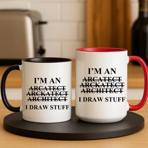Puede incluir: Dos tazas de cerámica blanca con asas negras. Las tazas tienen un borde negro y un borde rojo. Ambas tazas tienen el texto "I'M AN" y luego la palabra "ARCHITECT" escrita incorrectamente de tres maneras diferentes. El texto "I DRAW STUFF" está impreso debajo de las palabras mal escritas.