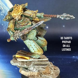 May include: A detailed miniature figure of a warrior in teal and gold armor, wielding a sword and a staff-like weapon. The figure stands on a rocky base. The text "US TARIFFS PREPAID ON ALL LISTINGS" is visible.