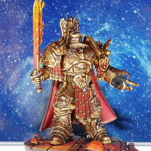 May include: A miniature figurine of a warrior clad in ornate gold armor with red accents, featuring a tall eagle-shaped crest on the back, a flowing red cape, and a flaming orange sword held in the right hand, standing on a textured base.