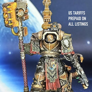 Pode incluir: Figura em miniatura detalhada de um guerreiro em armadura ornamentada, segurando um bastão com uma cabeça em forma de martelo. A figura é pintada em dourado metálico, preto e vermelho, com detalhes intrincados. O texto "US TARIFFS PREPAID ON ALL LISTINGS" é visível.