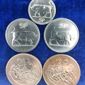 May include: A collection of British coins, including 5 pence and 2 pence pieces. The 5p coins feature a bull, while the 2p coins display an intricate design. The coins are silver and copper-colored, set against a dark blue background.