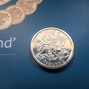May include: A silver British one pound coin with the inscription "ONE POUND" and a design of four heraldic beasts.