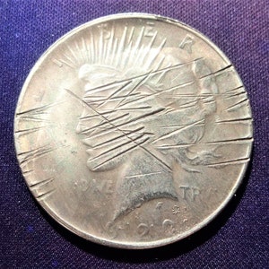 May include: A silver coin with a woman's profile, the word "LIBERTY" and the year 1922. The coin has multiple scratches across the face.