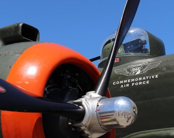 May include: A close-up of a vintage aircraft propeller with an orange and black engine cowling. The aircraft is painted green and has the text "COMMEMORATIVE AIR FORCE" on the side.
