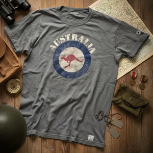 May include: A grey short-sleeved t-shirt featuring a distressed circular graphic with a blue border and a red kangaroo silhouette in the center. The word AUSTRALIA is printed in white capital letters in an arc above the circular emblem.