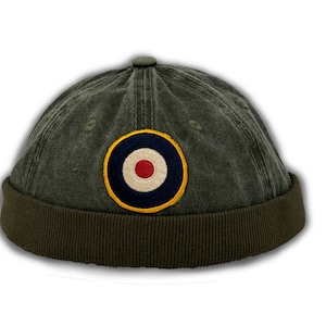 May include: A green cotton beanie with a round, navy blue, white, and red patch with a yellow border. The patch has a white circle in the center with a red dot.