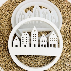 Könnte beinhalten: Weiße Silikonform zum Herstellen eines runden Harz-Anhängers mit einer Stadtlandschaft mit fünf Häusern. Die Form wird mit einem fertigen Anhänger gezeigt.