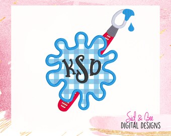 May include: Blue paint splatter with a gingham pattern and the monogram "K.S.D." in black. A red and gray paintbrush with a blue paint drop is beside the splatter.
