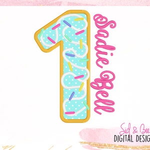 May include: A digital design featuring a number one shaped like a donut with blue frosting and sprinkles. The name "Sadie Bell" is written in pink script. The design is on a white background with a pink border.
