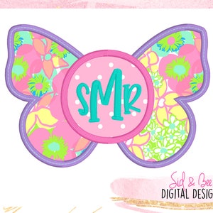 May include: A butterfly-shaped design with a floral pattern in pink, yellow, and green. The butterfly has a purple outline with a stitched effect. A pink circle in the center features the initials "SMR" in teal. The design is on a white background.