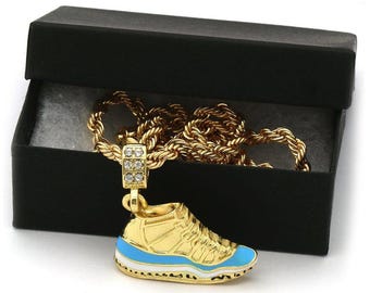 May include: A gold chain necklace with a gold pendant shaped like a basketball shoe with a blue and white design. The necklace is in a black velvet box.