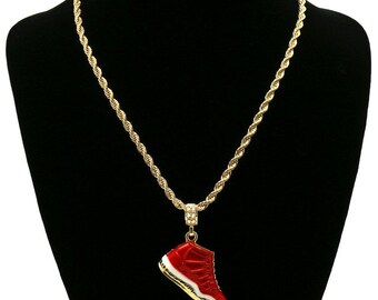 May include: Gold rope chain necklace with a red and white sneaker pendant. The pendant has a gold trim and a small amount of clear rhinestones.