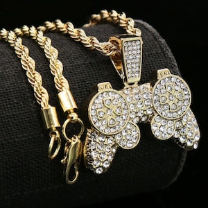 以下が含まれることがあります： ダイヤモンドで飾られたビデオゲームコントローラーの形をした大きなペンダントが付いたゴールドチェーンネックレス