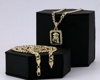 May include: A gold chain necklace with a square pendant featuring a detailed image of Jesus Christ with a crown of thorns. The pendant is set with clear cubic zirconia stones. The necklace is displayed on a black velvet box.