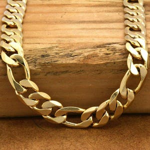 May include: A gold curb chain necklace with a thick, flat link design. The chain is made of a shiny metal and has a smooth finish.
