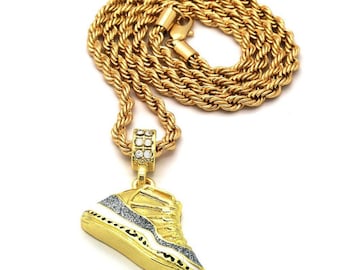May include: Gold rope chain necklace with a gold sneaker pendant featuring a white and black design and clear cubic zirconia stones.