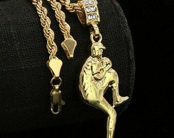 May include: A gold chain necklace with a gold pendant featuring a baseball player in a pitching pose. The pendant is adorned with clear cubic zirconia stones.