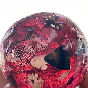 May include: A pink glass paperweight with white, black, and blue swirls and bubbles inside.