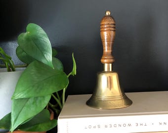 May include: A brass bell with a wooden handle. The bell is sitting on a stack of books with the text "NK THE WONDER SPOT" visible on the top book.