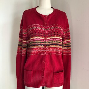 May include: Red cardigan sweater with a colorful geometric pattern and button closure. The sweater has two pockets on the front.