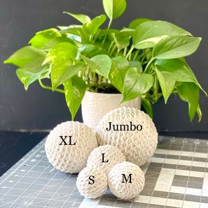 May include: Five white crocheted balls of different sizes, labeled "Jumbo", "XL", "L", "M", and "S".
