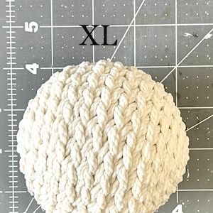 May include: A white, round, crocheted rope ball with a woven pattern. The ball is labeled "XL".