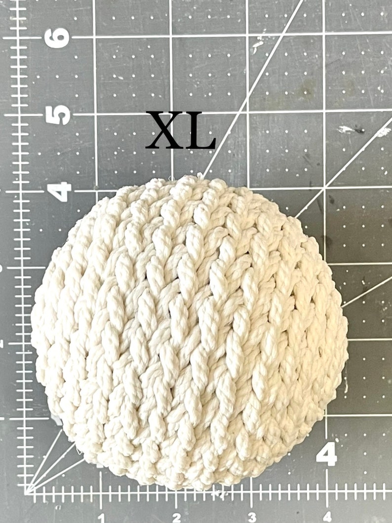 May include: A white, round, crocheted rope ball with a woven pattern. The ball is labeled "XL".
