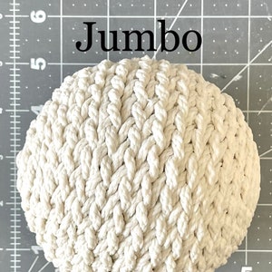 May include: A large, white, crocheted rope ball. The ball is made of thick, braided rope and has a textured surface. The ball is labeled "Jumbo".