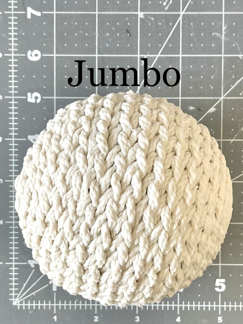 May include: A large, white, crocheted rope ball. The ball is made of thick, braided rope and has a textured surface. The ball is labeled "Jumbo".