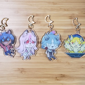May include: Four colorful anime character keychains with gold moon-shaped clasps. The characters are a blue wolf, a pink wolf, a blue wolf with a microphone, and a yellow three-headed wolf.