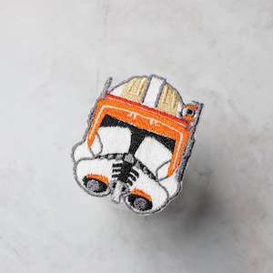 Puede incluir: Parche bordado de un casco de soldado clon de Star Wars blanco y naranja.