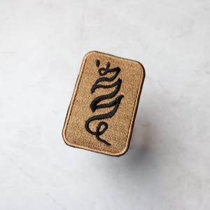 May include: A tan fabric patch with black embroidered lettering that reads "Envy".