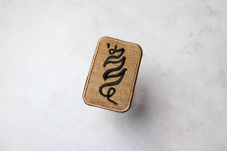 May include: A tan fabric patch with black embroidered lettering that reads "Envy".