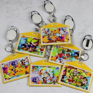 May include: Seven yellow retractable badge holders with colourful cartoon character designs. Each holder has a silver swivel clip and a white retractable cord.
