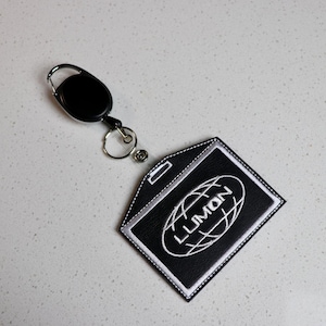 May include: Black retractable badge holder with a white embroidered logo that says "LLIMON" inside a circle.