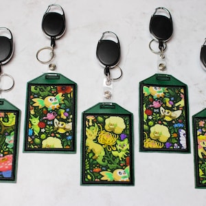May include: Five green and black retractable badge holders with colorful cartoon images of mythical creatures. Each badge holder has a black retractable cord and a metal clip.