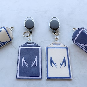 May include: Two white and two blue hand sanitizer holders with a blue and white embroidered design. Each holder has a silver retractable keychain.