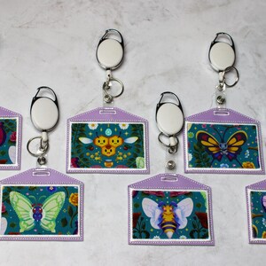 Pode incluir: Seis porta-crachás roxos com carretéis retráteis para crachás. Cada porta-crachá apresenta um design colorido diferente com um motivo de borboleta ou abelha.