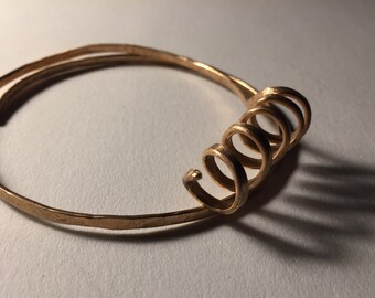 Bronze cuff bracelet with coiled symbol.