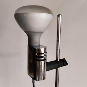 May include: A chrome floor lamp with a white bulb and a black adjustable arm. The lamp has a chrome base and a chrome pole.