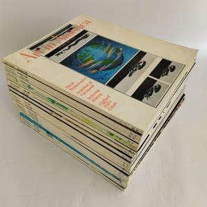 May include: A stack of vintage Art in America magazines from 1980. The cover of the top magazine features a colorful illustration of the Earth with ships and planes traveling around it. The text on the cover reads "Art in America, December 1980, No. 12."