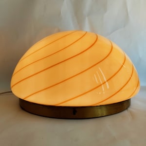 May include: A white and gold ceiling lamp with a dome-shaped shade featuring a swirling pattern of orange lines.