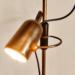 Könnte beinhalten: Eine goldfarbene Stehlampe mit schwarzem Akzent und einer weißen Glühbirne. Die Lampe hat einen flexiblen Arm und einen runden Sockel.