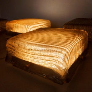 May include: Several illuminated, square-shaped glass blocks with a textured, ridged surface. The blocks are lit from within, casting a warm, golden glow. The design suggests a modern or art deco style, suitable for home decor.