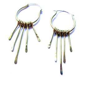 May include: A pair of gold hoop earrings with dangling strands of metal. The strands are thin and have a slightly rounded end.