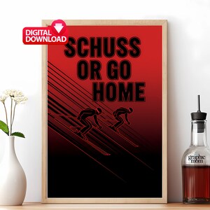May include: A framed poster with a red and black gradient background. The poster features the text "SCHUSS OR GO HOME" in bold black letters, along with a graphic of two skiers. A "DIGITAL DOWNLOAD" icon is in the upper left corner.