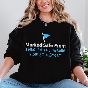 May include: Black sweatshirt with the text "Marked Safe From Being On The Wrong Side Of History" in white and blue. A blue flag graphic is above the text. The sweatshirt is worn by a person wearing blue jeans.