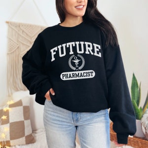 May include: Black sweatshirt with white text that reads "FUTURE PHARMACIST" with a caduceus symbol inside a laurel wreath.