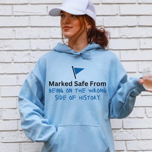 Puede incluir: Una sudadera con capucha azul claro con un gráfico de bandera azul y el texto "Marked Safe From Being on the Wrong Side of History".