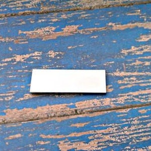 Puede incluir: Un letrero rectangular blanco sobre una superficie de madera azul y marrón. La superficie está desgastada y tiene un aspecto rústico.